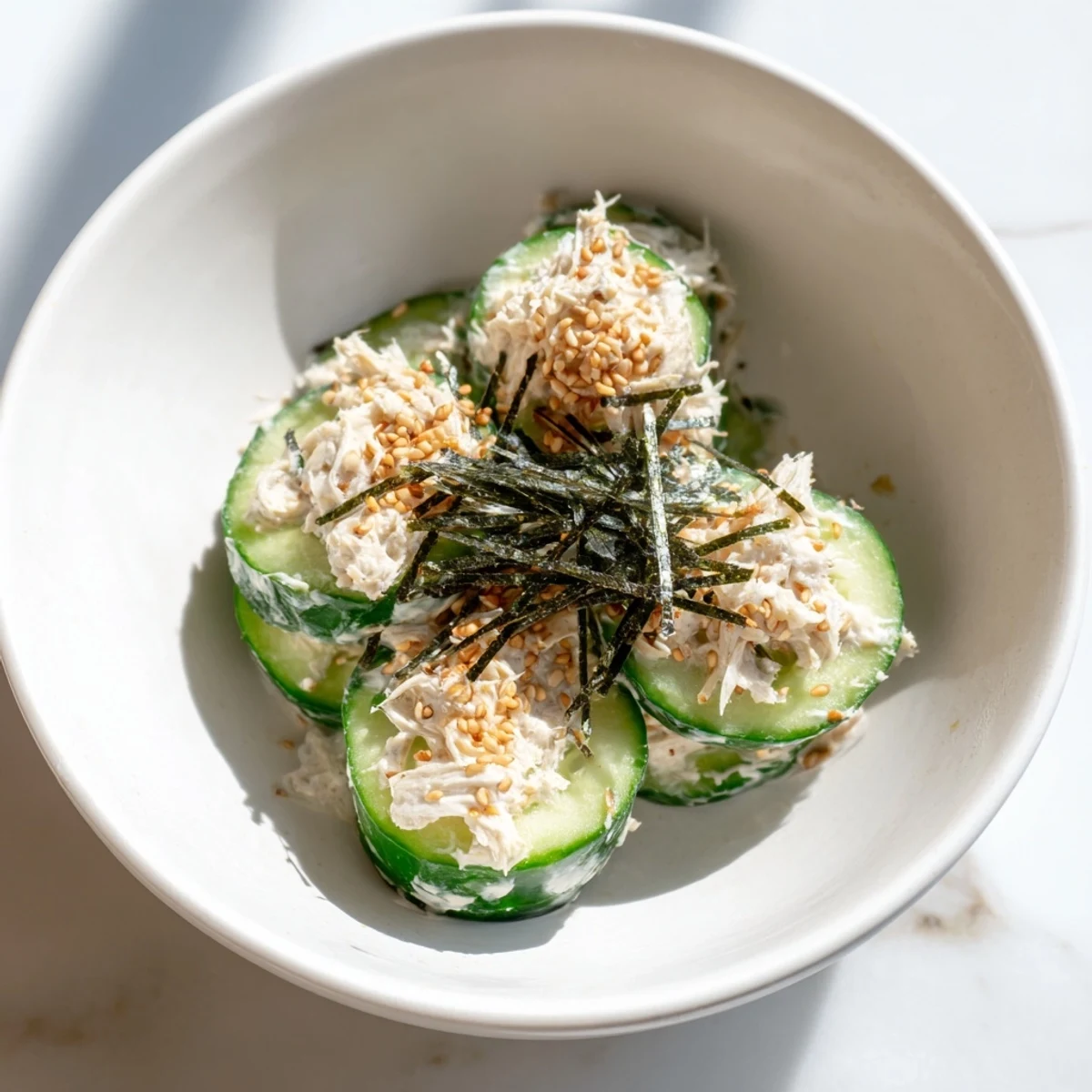 California Roll Cucumber Salad topped with nori strips and pickled ginger served in a white ceramic bowl.