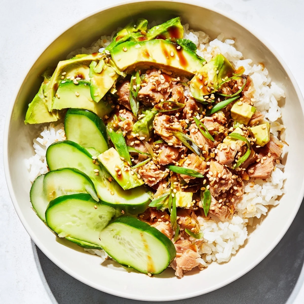 Savory Tuna Avocado Rice Bowl brimming with flaky tuna, creamy avocado slices, and crisp cucumber atop warm jasmine rice, finished with toasted sesame seeds.  