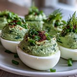 Fresh green avocado deviled eggs with creamy filling, garnished with herbs and paprika for a vibrant spring appetizer.  