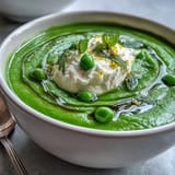 A vibrant bowl of Spring Pea Soup with whipped ricotta and mint oil, garnished with fresh peas and mint leaves.  