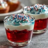 Colorful alcohol-free Firecracker Jello Shots with whipped cream and sprinkles, ready for enjoyment.