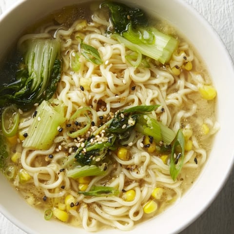 A steaming bowl of Elevated Ramen Egg Drop Soup features silky egg ribbons and tender noodles in a creamy broth.
