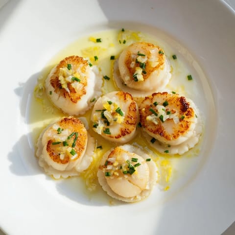 Perfectly cooked pan-seared scallops, a beautiful main course, served with lemon wedges and sauce.
