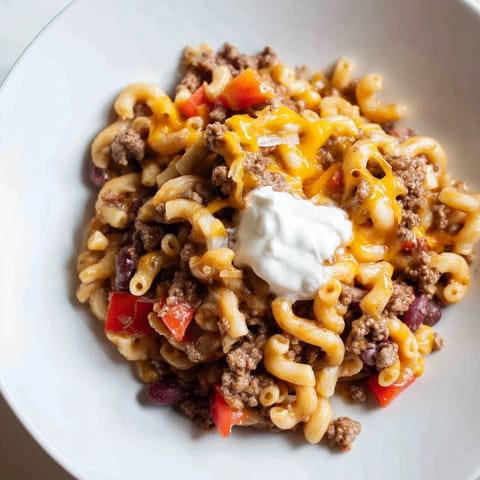 A steaming bowl of One-Pot Chili Mac shows a creamy tomato sauce with pasta and ground beef.