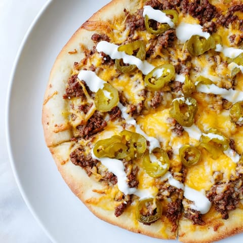 Close-up of a fully-loaded, bubbly Ground Beef Taco Pizza ready to be sliced and devoured.