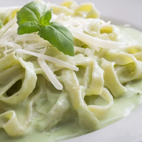 A close-up of Creamy Green Pea Alfredo highlights silky Parmesan sauce and sweet peas in fettuccine, ready for a comforting dinner.  