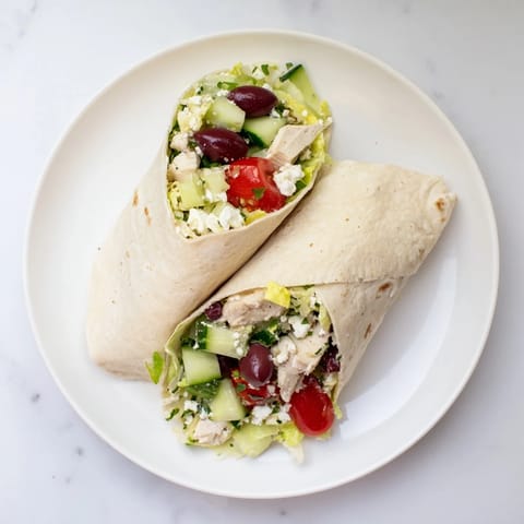 A close-up of a Greek Lemon Chicken Salad Wrap, showcasing juicy marinated chicken, cherry tomatoes, cucumber, and crumbled feta inside a warm, folded tortilla.  