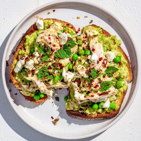 Golden, crispy sourdough toast topped with creamy smashed pea and tender shredded chicken mixture, garnished with fresh herbs and a sprinkle of chili flakes.